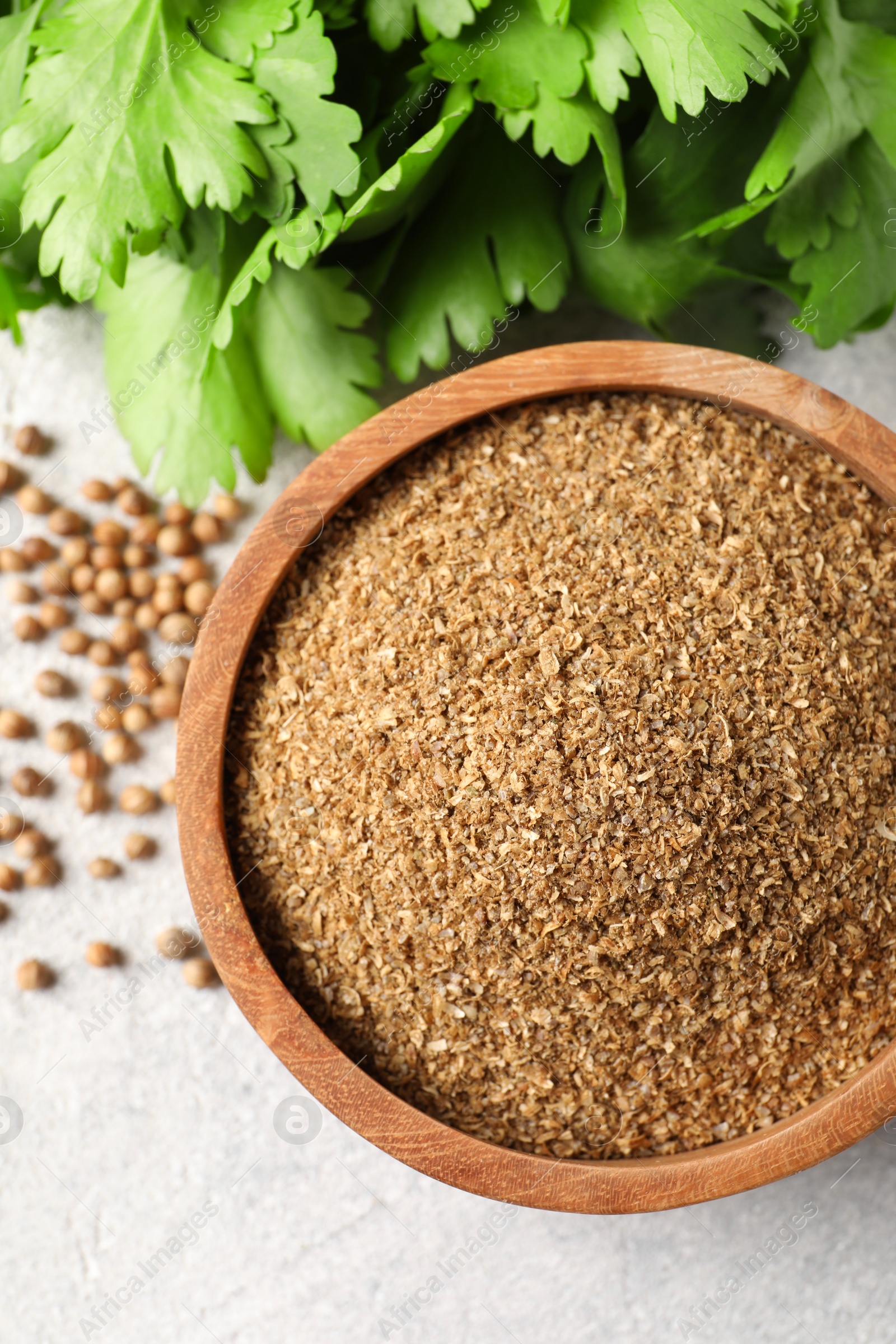 Photo of Coriander powder in bowl, green leaves and seeds on light grey table, top view