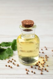 Photo of Coriander essential oil, seeds and green leaves on wooden table