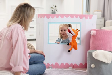 Photo of Puppet theatre. Smiling girl performing show with toy to her mother at home