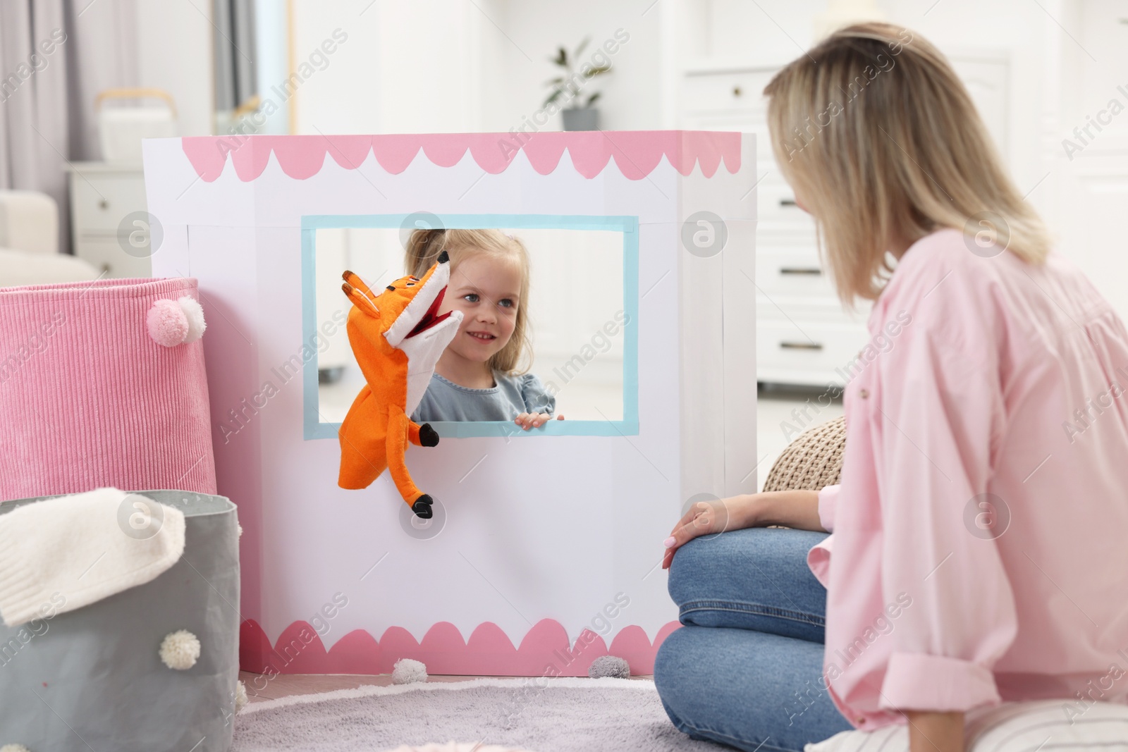 Photo of Puppet theatre. Smiling girl performing show with toy to her mother at home