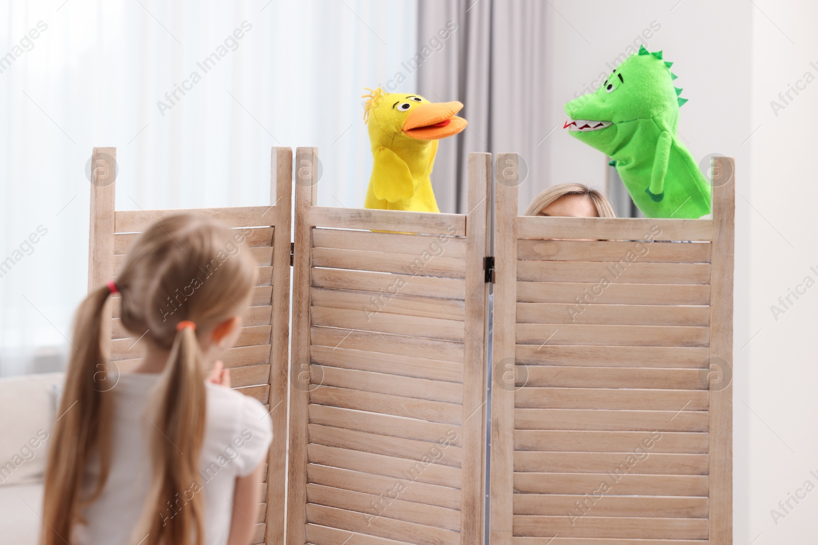 Photo of Girl watching puppet theatre at home, back view