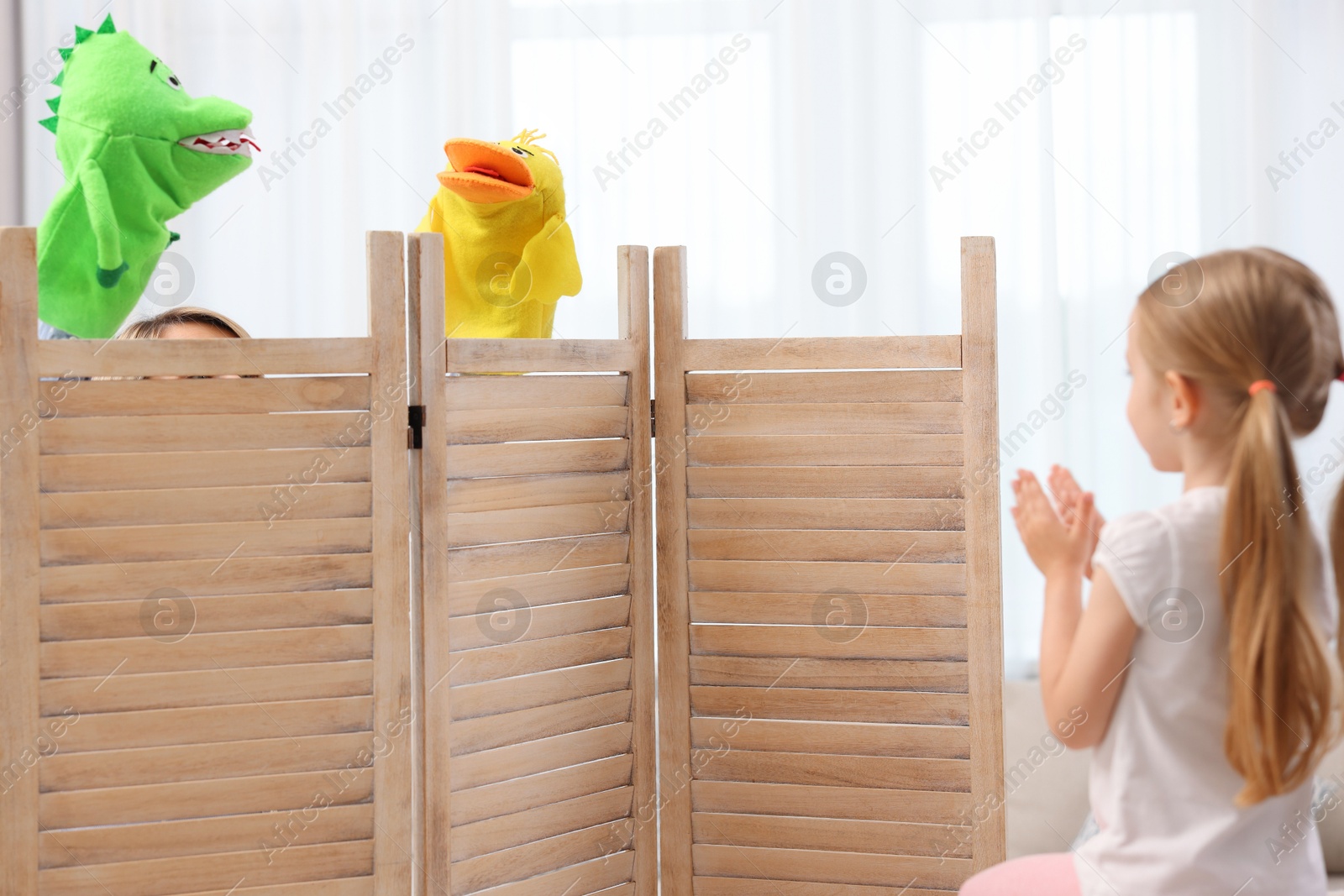 Photo of Girl watching puppet theatre at home, back view