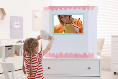 Photo of Puppet theatre. Smiling mother performing show with toys to her daughter at home