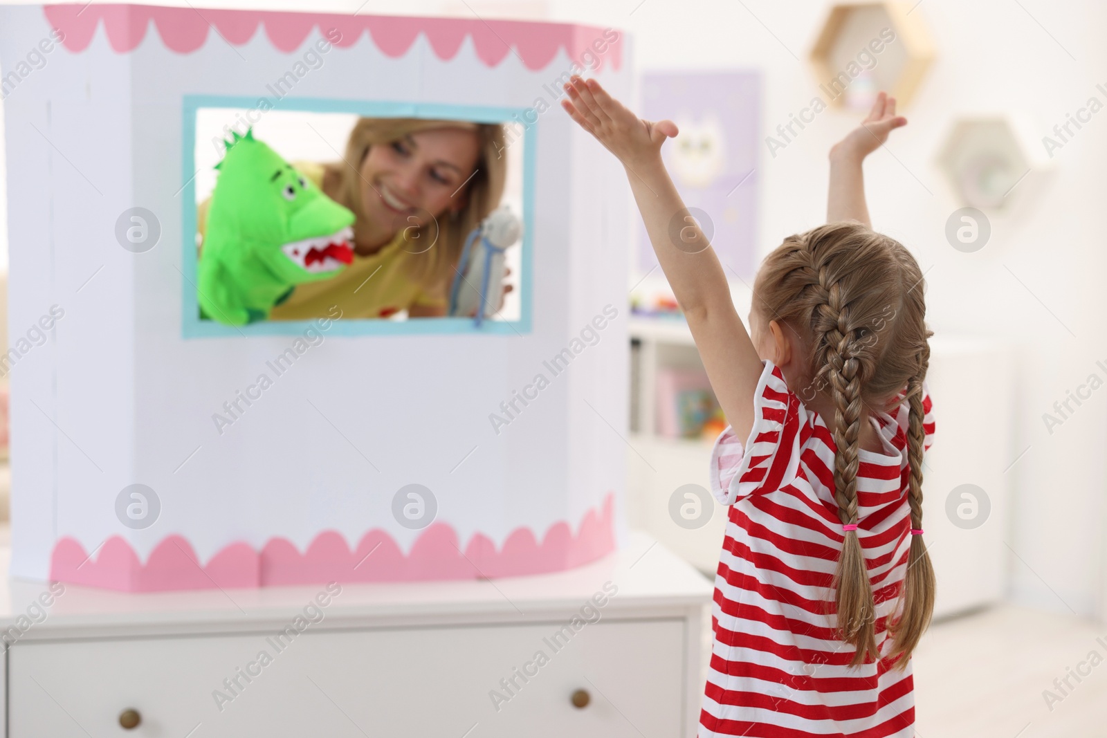 Photo of Puppet theatre. Smiling mother performing show with toys to her daughter at home, selective focus