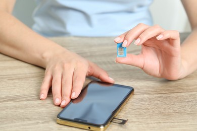 Woman holding SIM card near smartphone at wooden table, closeup