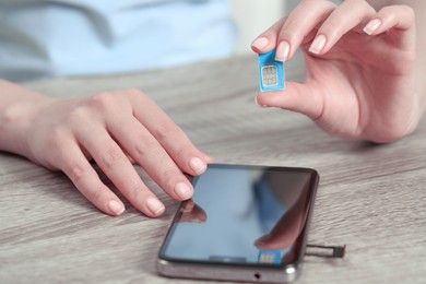 Woman holding SIM card near smartphone at wooden table, closeup