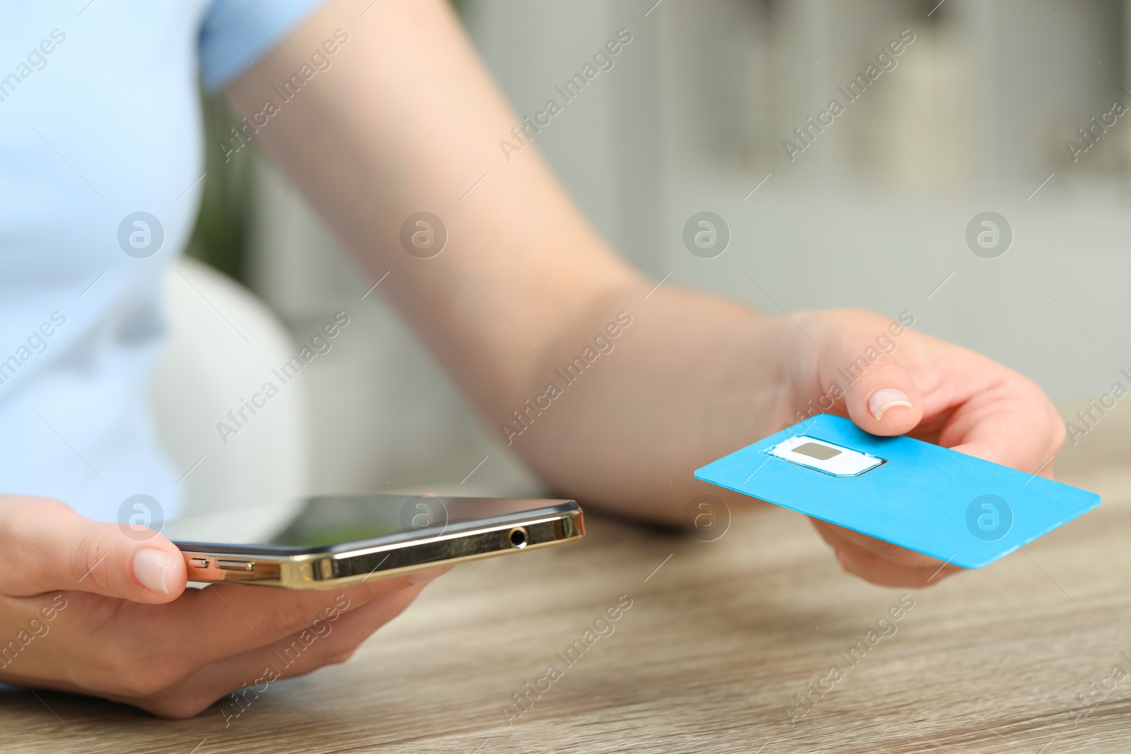 Photo of Woman holding SIM card and smartphone at wooden table indoors, closeup