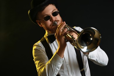 Photo of Professional musician playing trumpet on black background in color lights