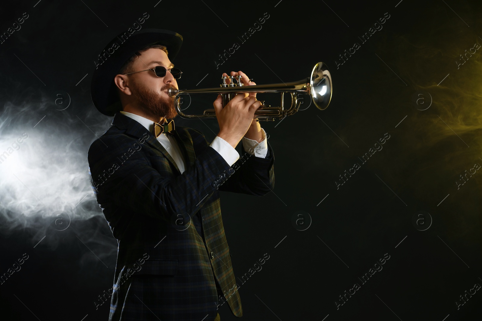 Photo of Professional musician playing trumpet on black background in color lights and smoke. Space for text