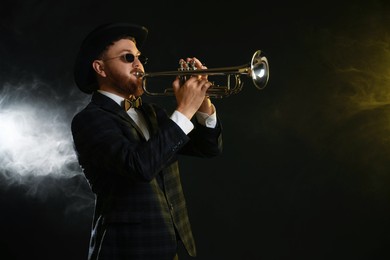 Photo of Professional musician playing trumpet on black background in color lights and smoke. Space for text