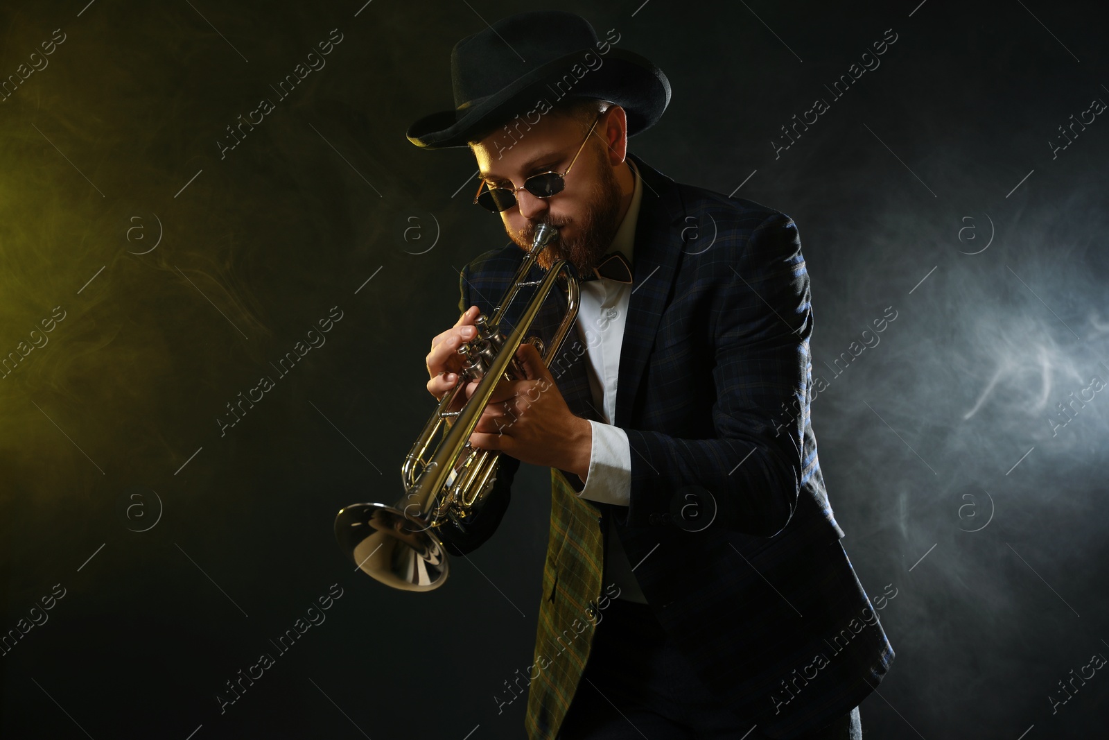 Photo of Professional musician playing trumpet on black background in color lights and smoke