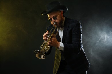 Professional musician playing trumpet on black background in color lights and smoke