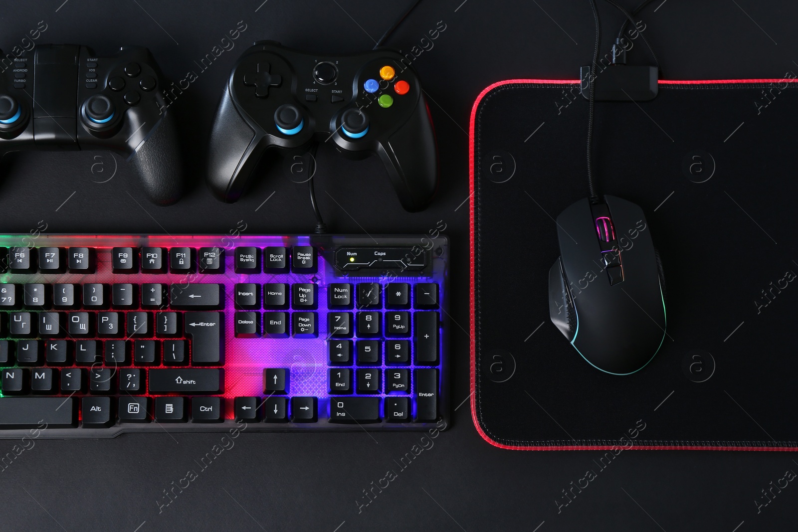 Photo of Computer mouse, RGB keyboard and game controllers on black background, top view