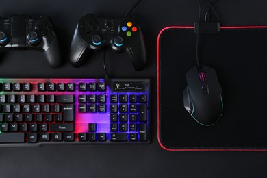 Computer mouse, RGB keyboard and game controllers on black background, top view