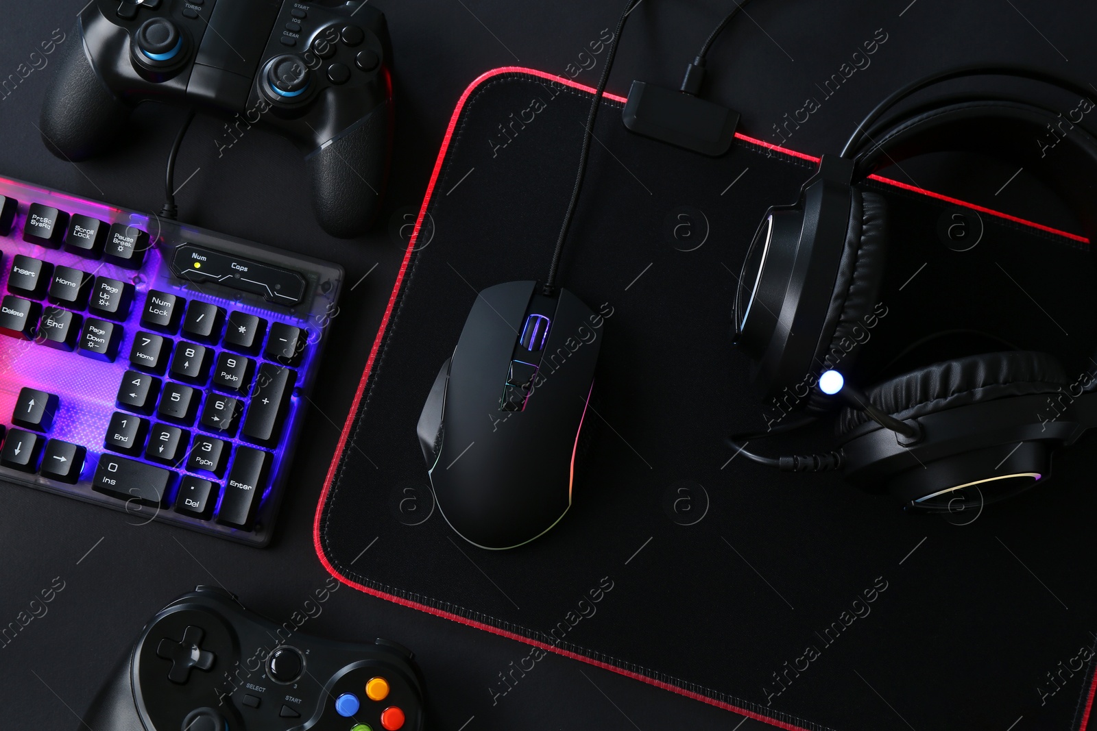 Photo of Computer mouse, RGB keyboard, game controllers and headset on black background, top view