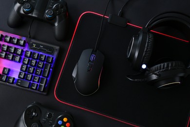 Photo of Computer mouse, RGB keyboard, game controllers and headset on black background, top view