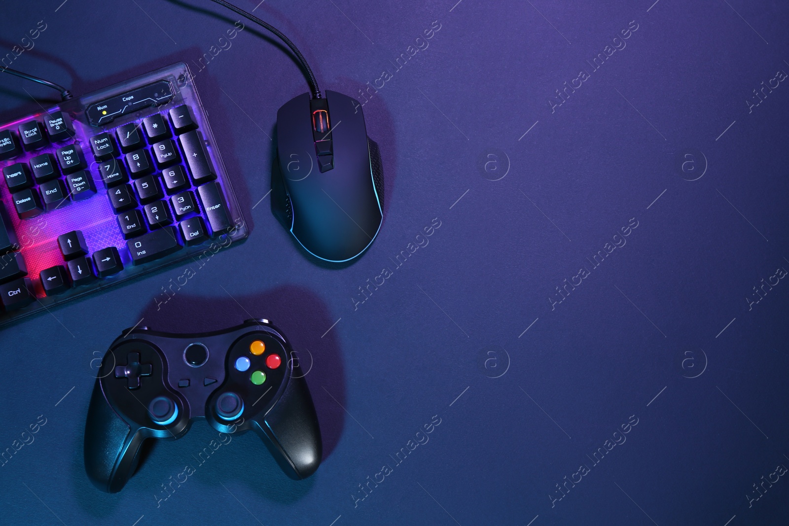 Photo of Computer mouse, RGB keyboard and game controller on dark background, flat lay. Space for text