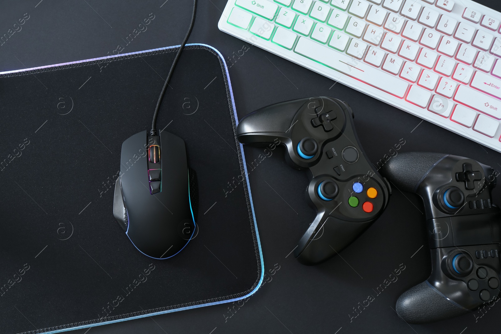 Photo of Computer mouse, RGB keyboard and game controllers on black background, top view