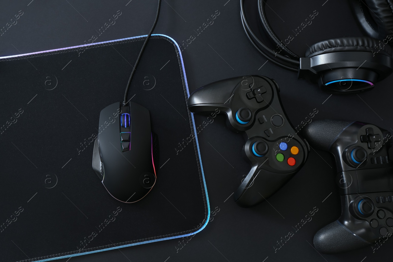 Photo of Computer mouse, mousepad, headset and game controllers on black background, flat lay