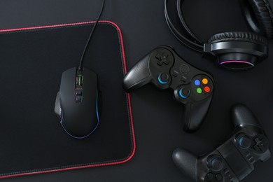 Photo of Computer mouse, mousepad, headset and game controllers on black background, flat lay