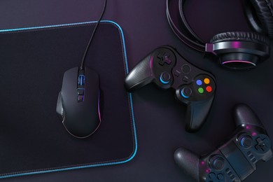 Computer mouse, mousepad, headset and game controllers on black background, flat lay