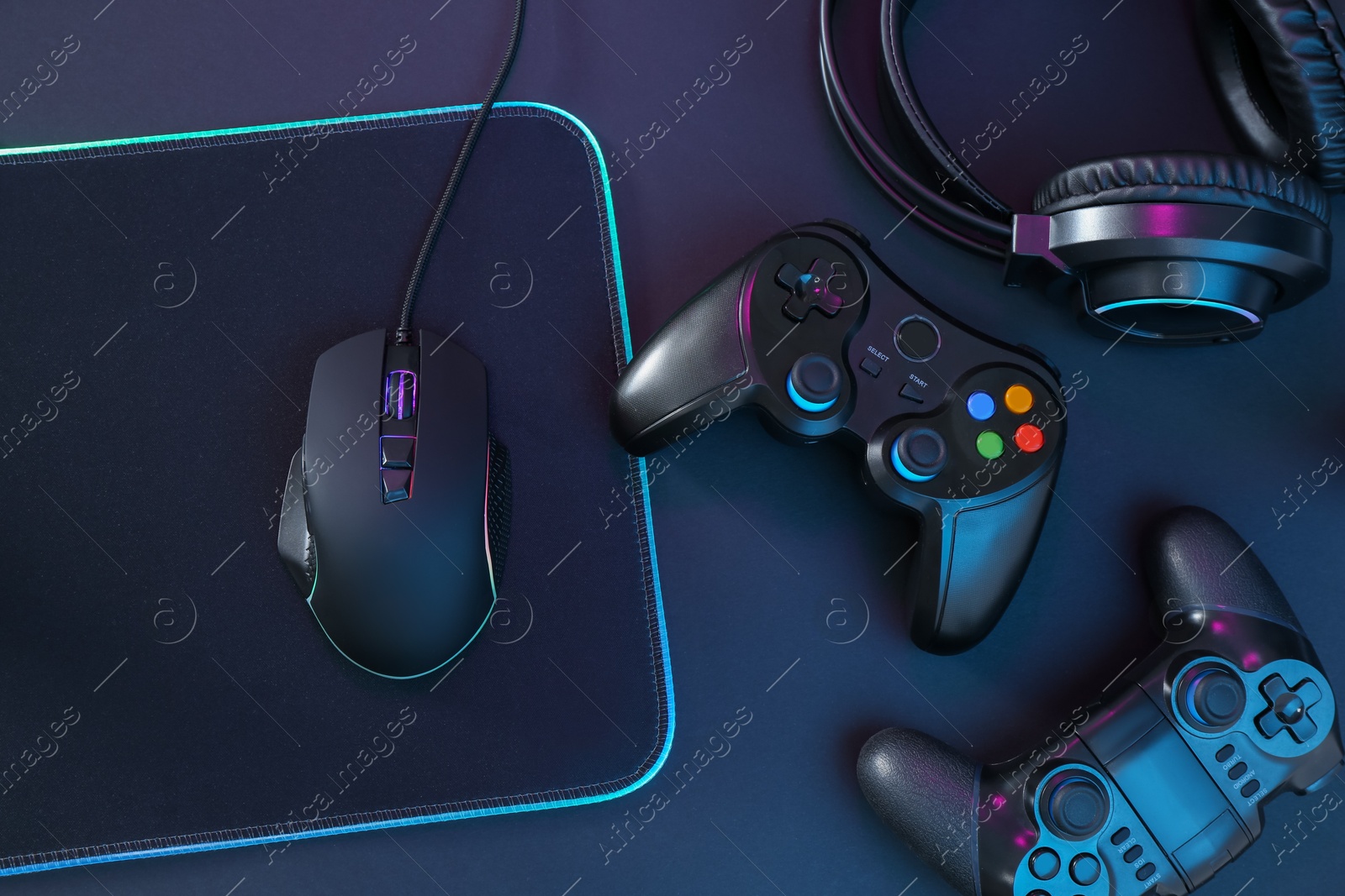 Photo of Computer mouse, mousepad, headset and game controllers on black background, flat lay