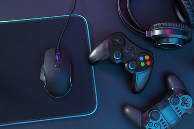 Photo of Computer mouse, mousepad, headset and game controllers on black background, flat lay