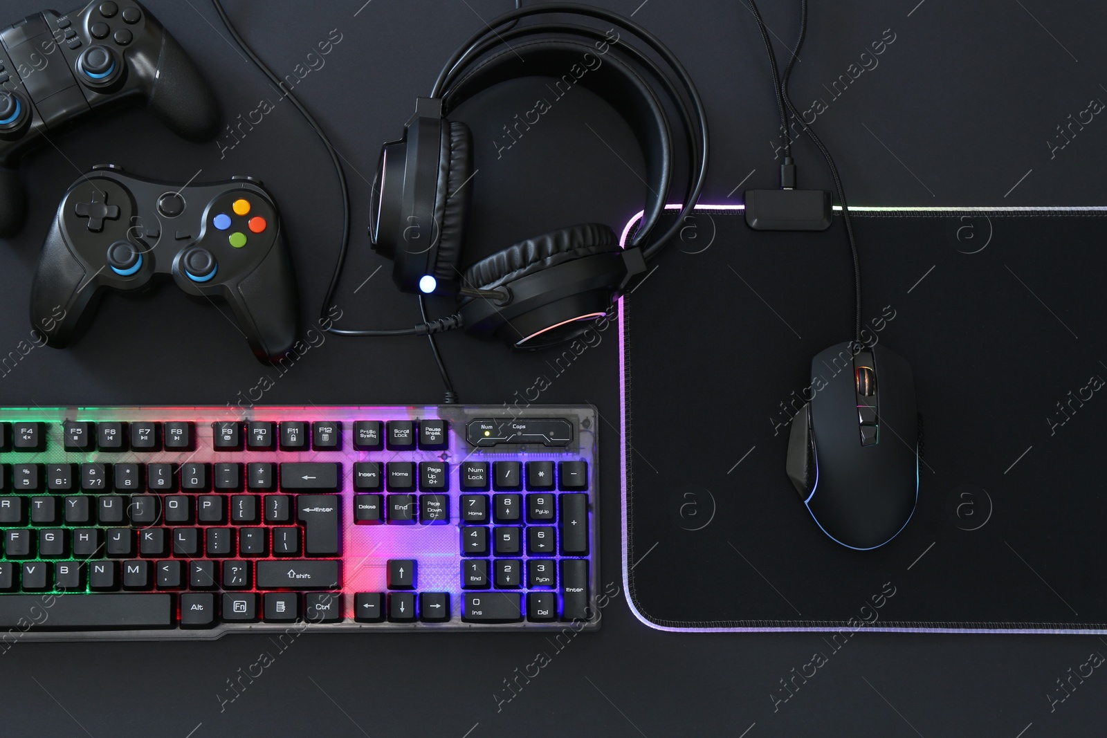 Photo of Computer mouse, RGB keyboard, headset and game controllers on black background, top view