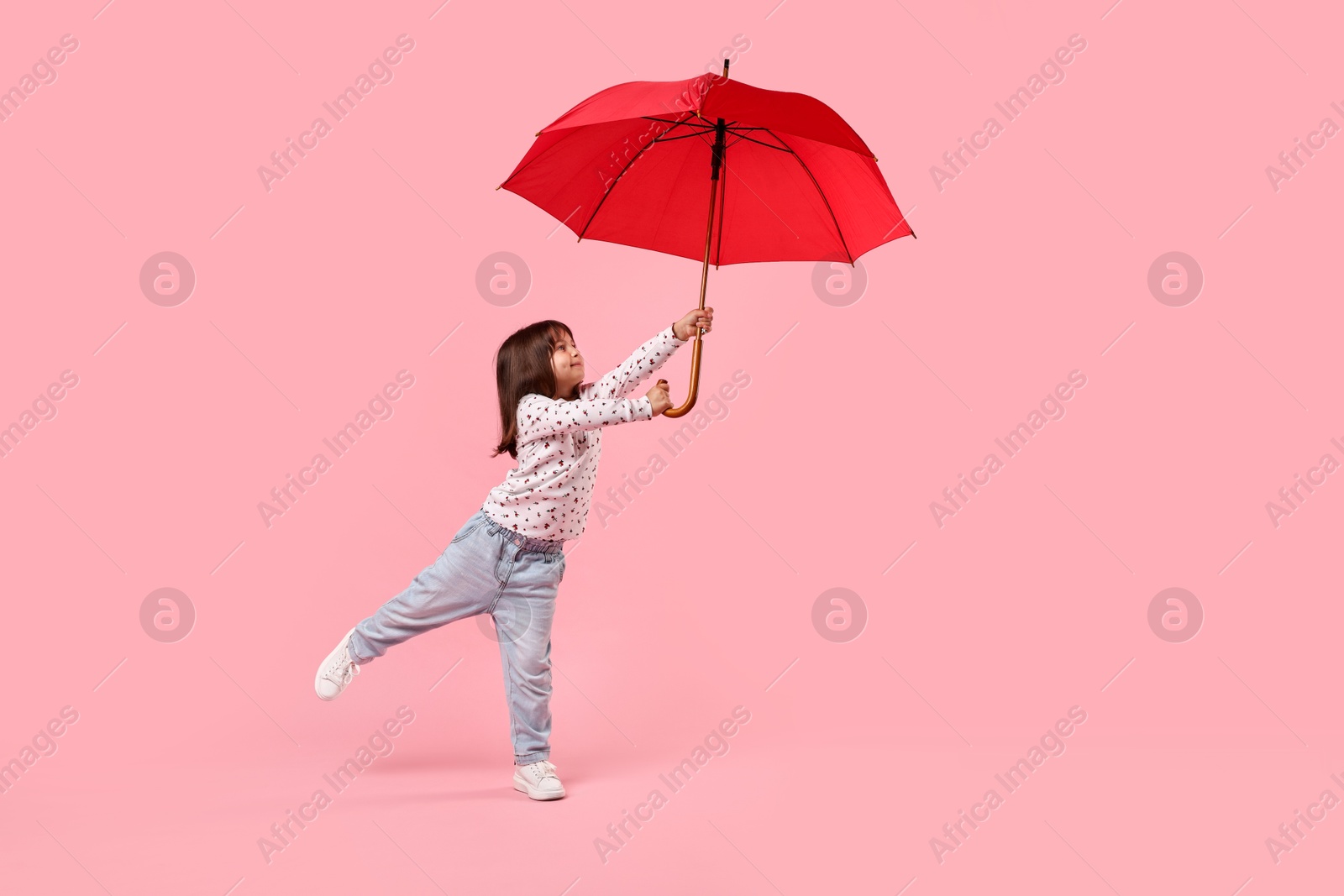 Photo of Cute little girl with red umbrella on pink background