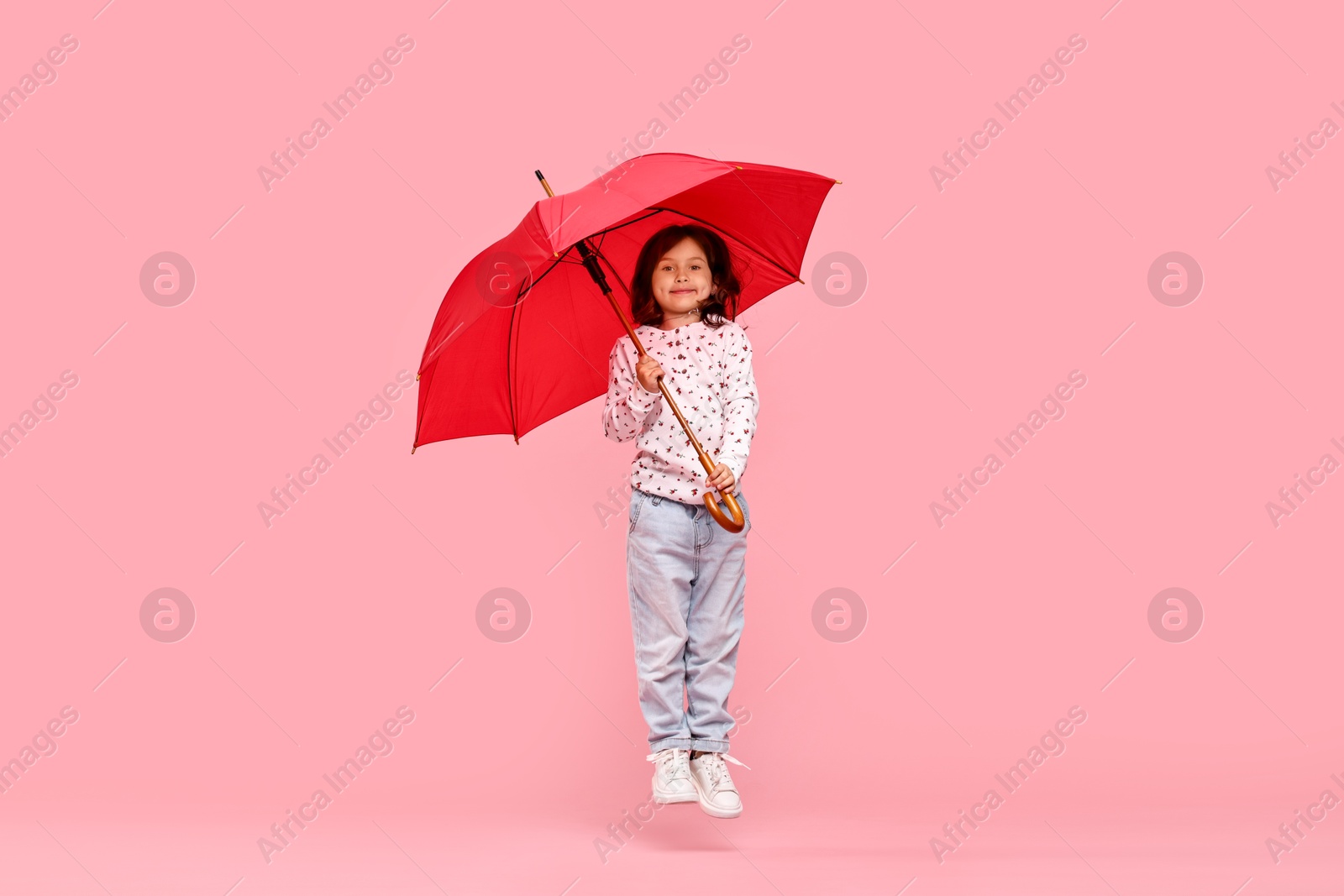 Photo of Cute little girl with red umbrella on pink background