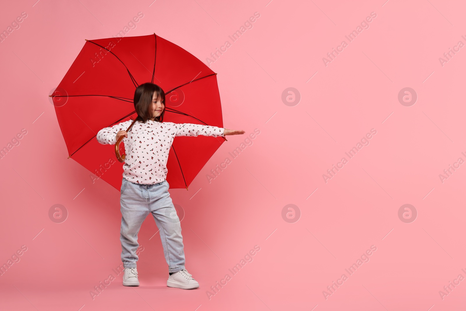 Photo of Cute little girl with red umbrella on pink background. Space for text