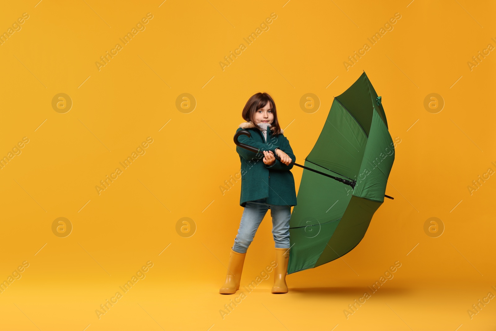 Photo of Cute little girl with green umbrella on yellow background. Space for text