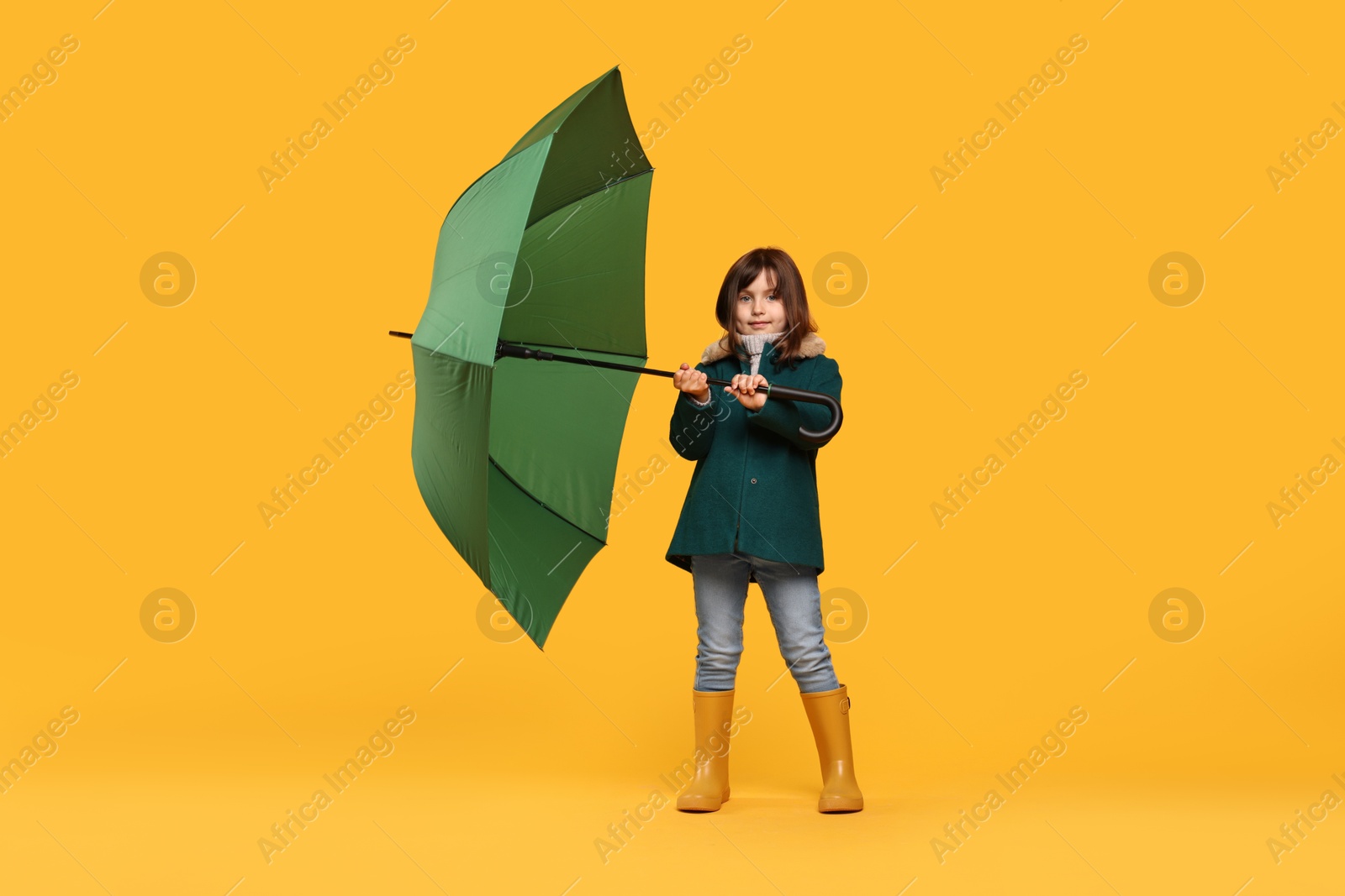 Photo of Cute little girl with green umbrella on yellow background