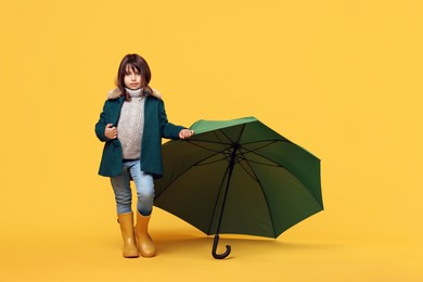 Photo of Cute little girl with green umbrella on yellow background