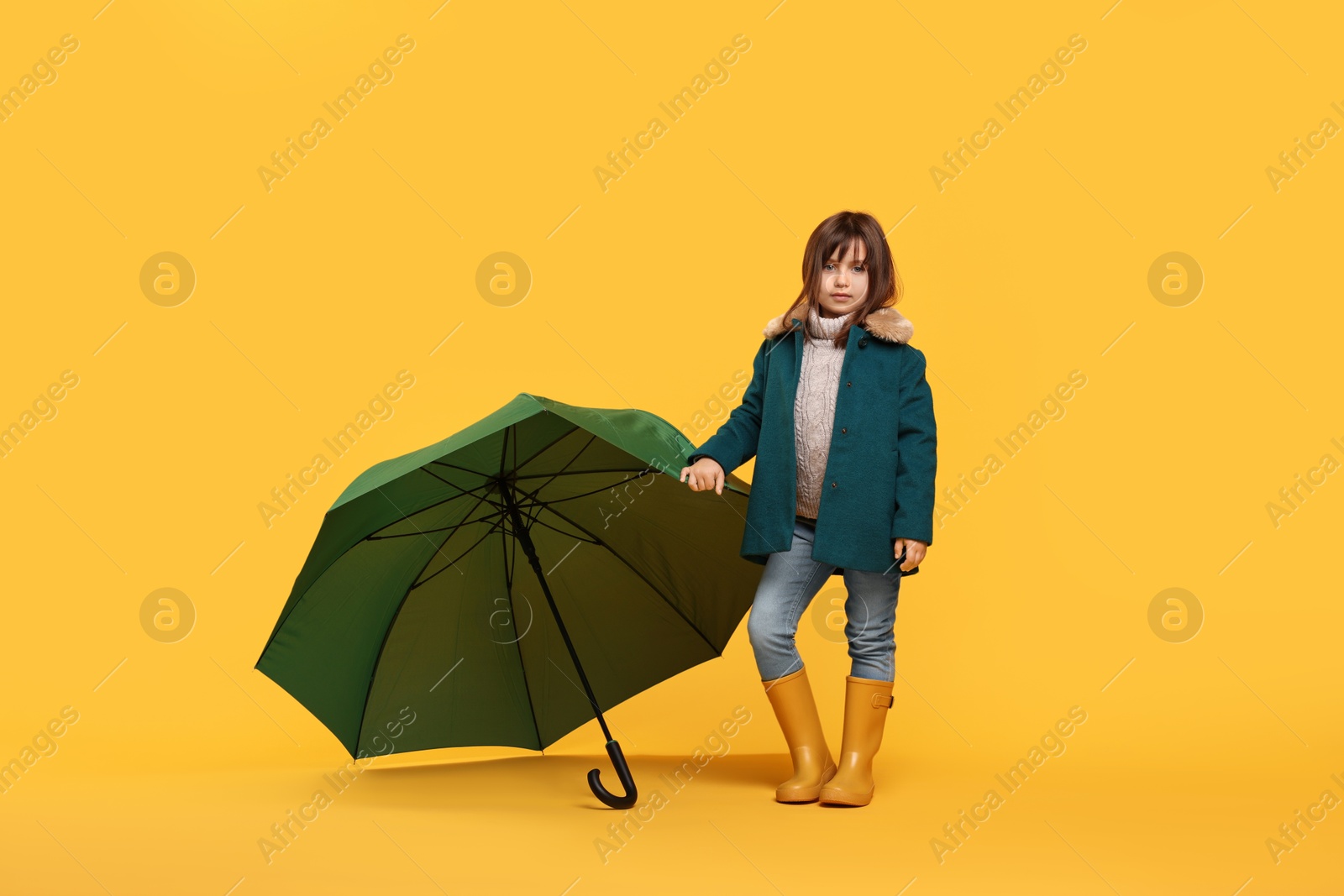 Photo of Cute little girl with green umbrella on yellow background