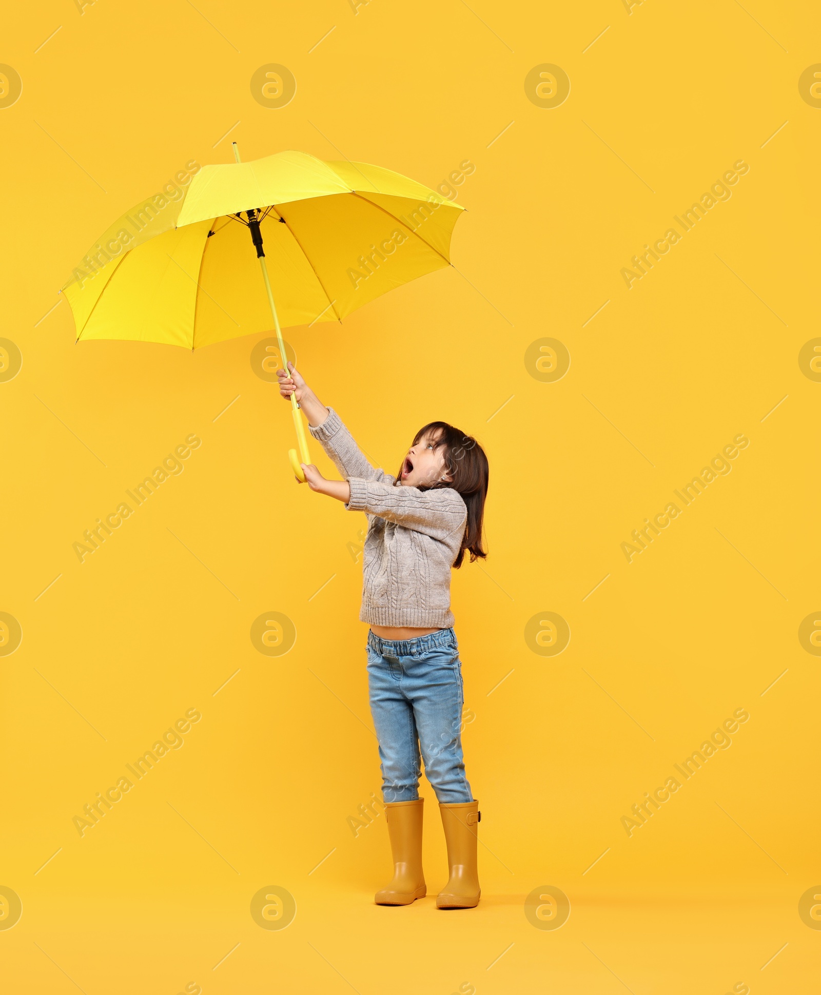 Photo of Cute little girl with bright umbrella on yellow background. Space for text