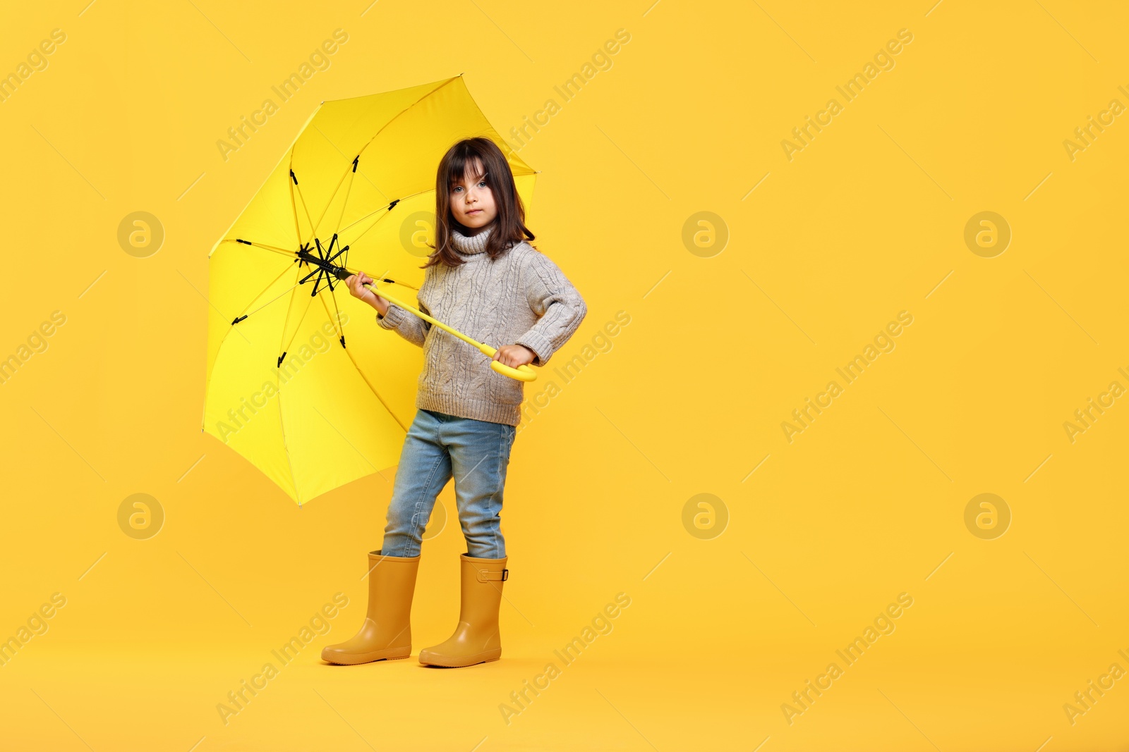 Photo of Cute little girl with bright umbrella on yellow background. Space for text