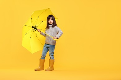 Cute little girl with bright umbrella on yellow background. Space for text