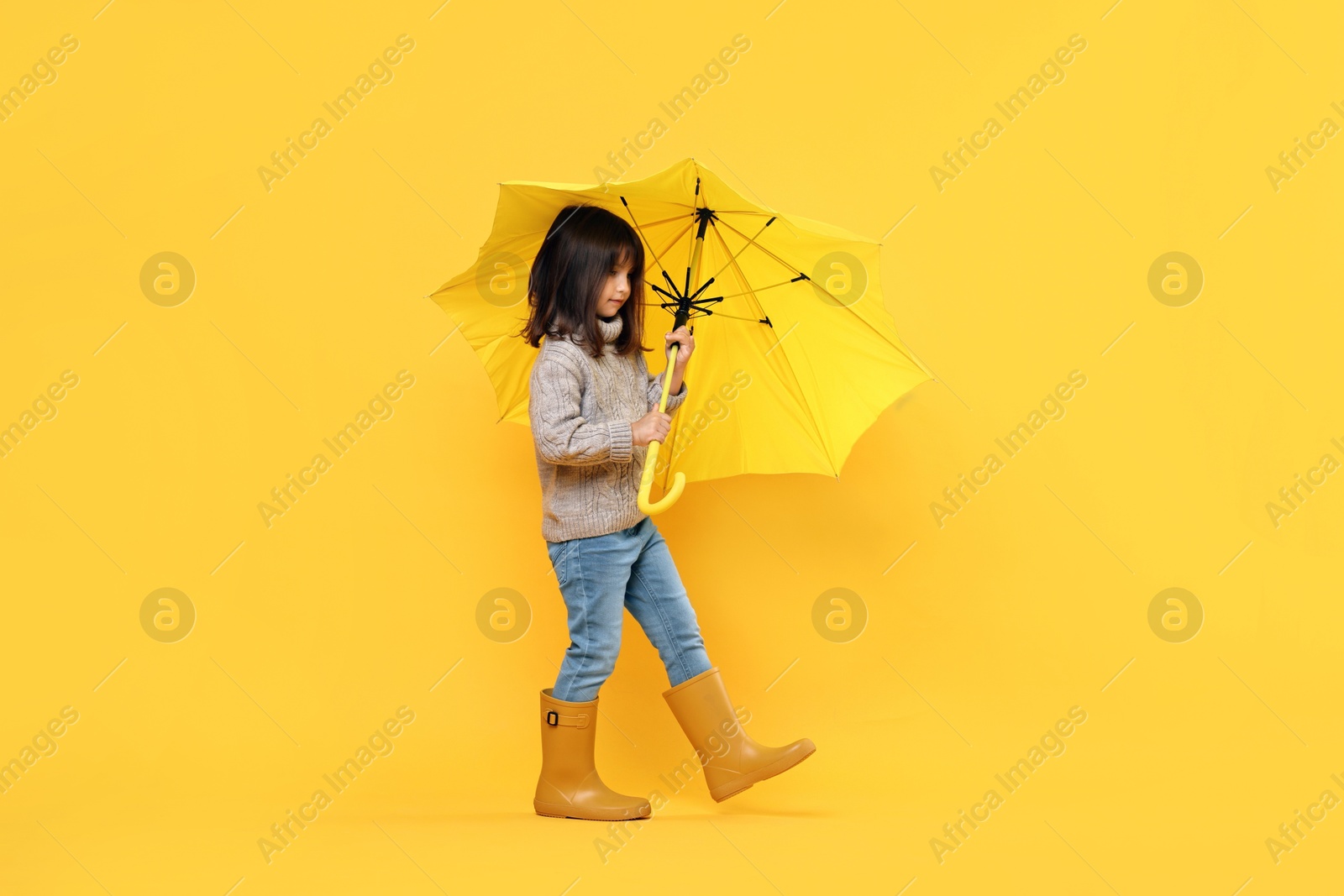 Photo of Cute little girl with bright umbrella on yellow background