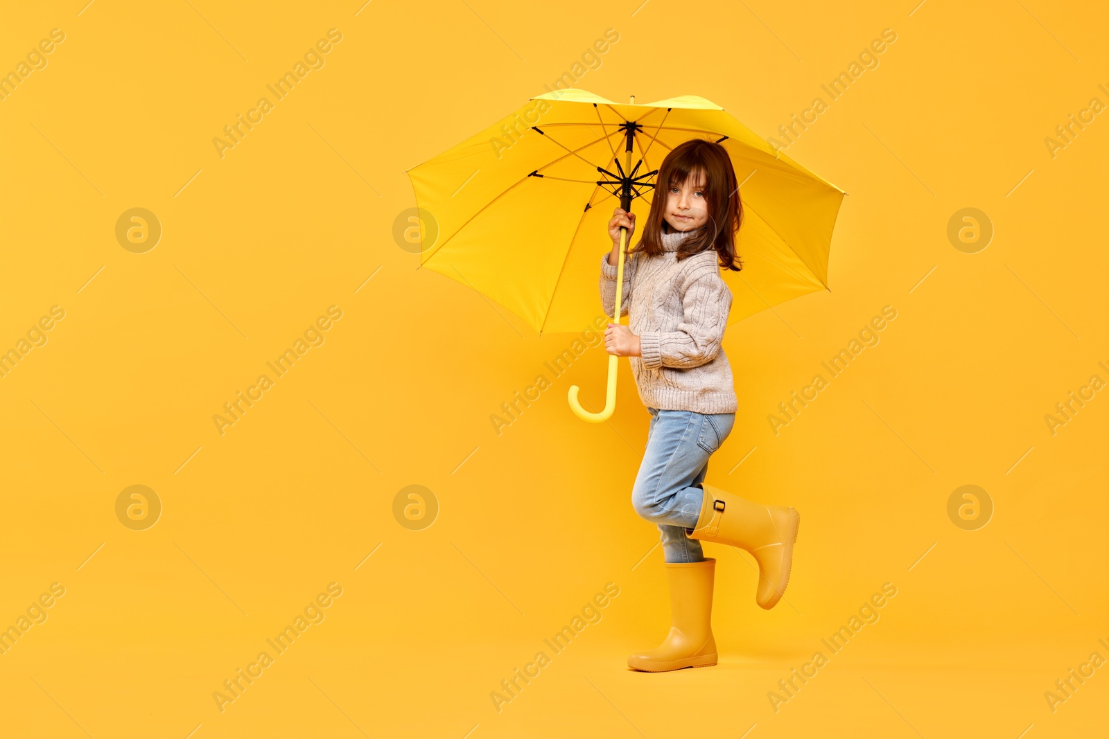 Photo of Cute little girl with bright umbrella on yellow background. Space for text