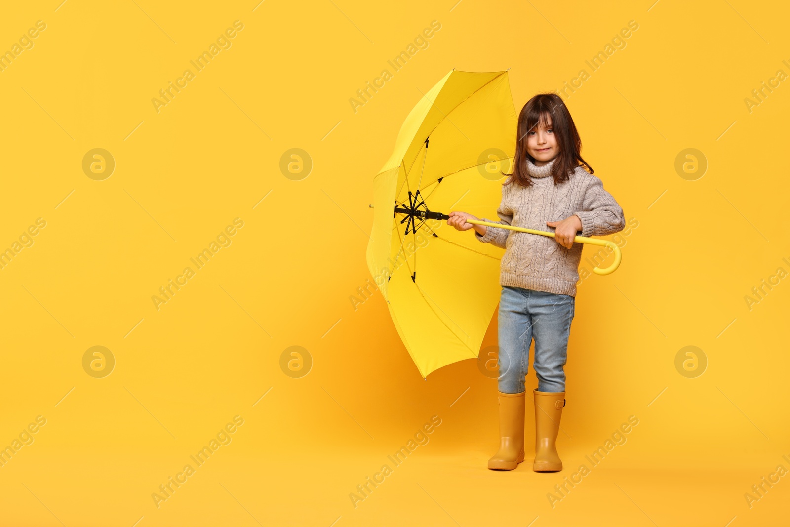 Photo of Cute little girl with bright umbrella on yellow background. Space for text