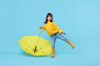 Photo of Cute little girl with yellow umbrella on light blue background