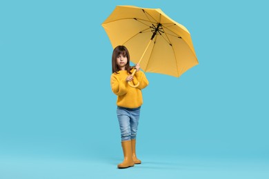 Photo of Cute little girl with yellow umbrella on light blue background