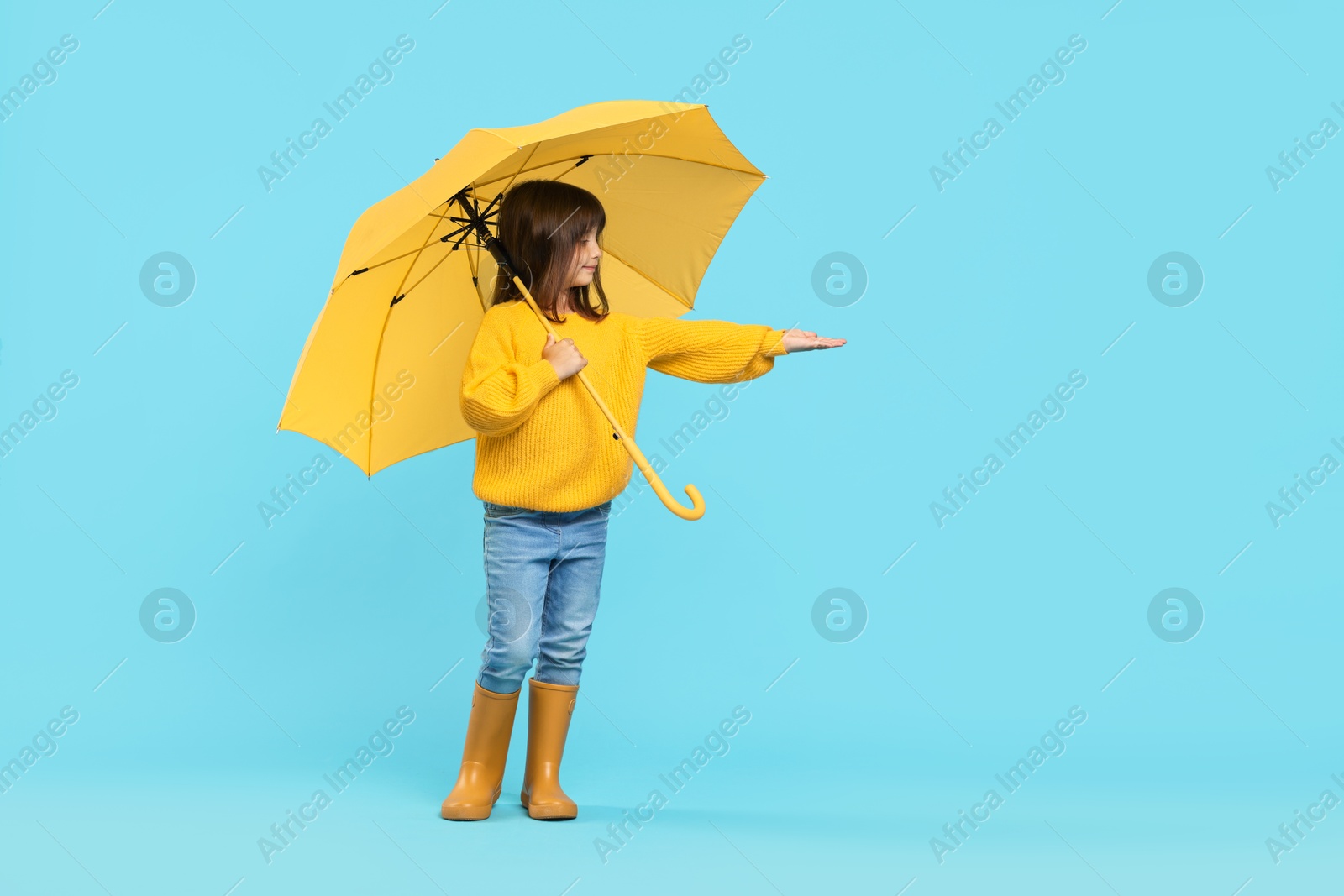 Photo of Cute little girl with yellow umbrella on light blue background. Space for text