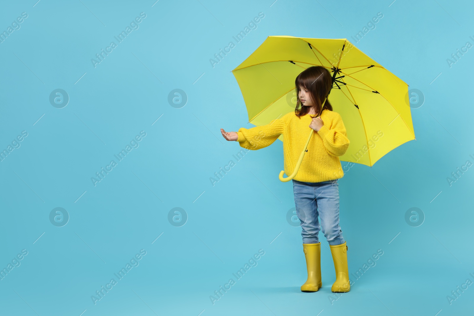 Photo of Cute little girl with yellow umbrella on light blue background. Space for text