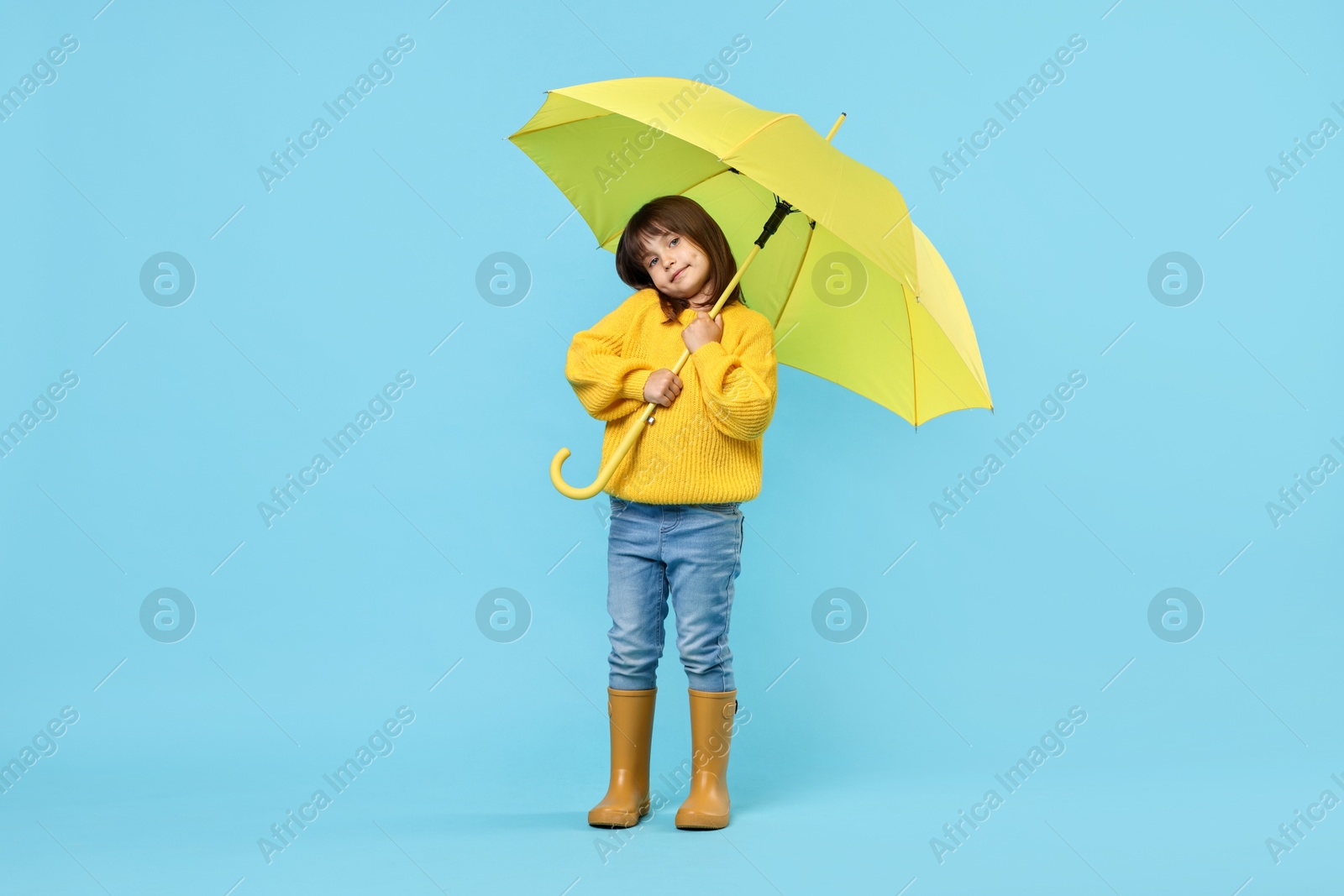 Photo of Cute little girl with yellow umbrella on light blue background