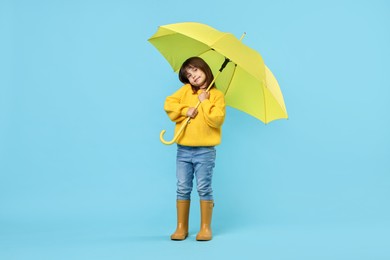 Cute little girl with yellow umbrella on light blue background