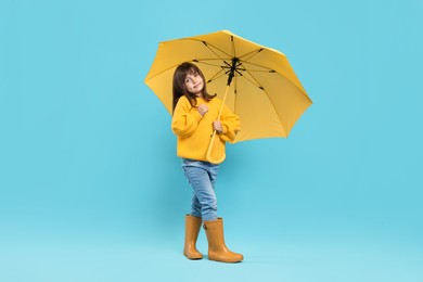 Photo of Cute little girl with yellow umbrella on light blue background