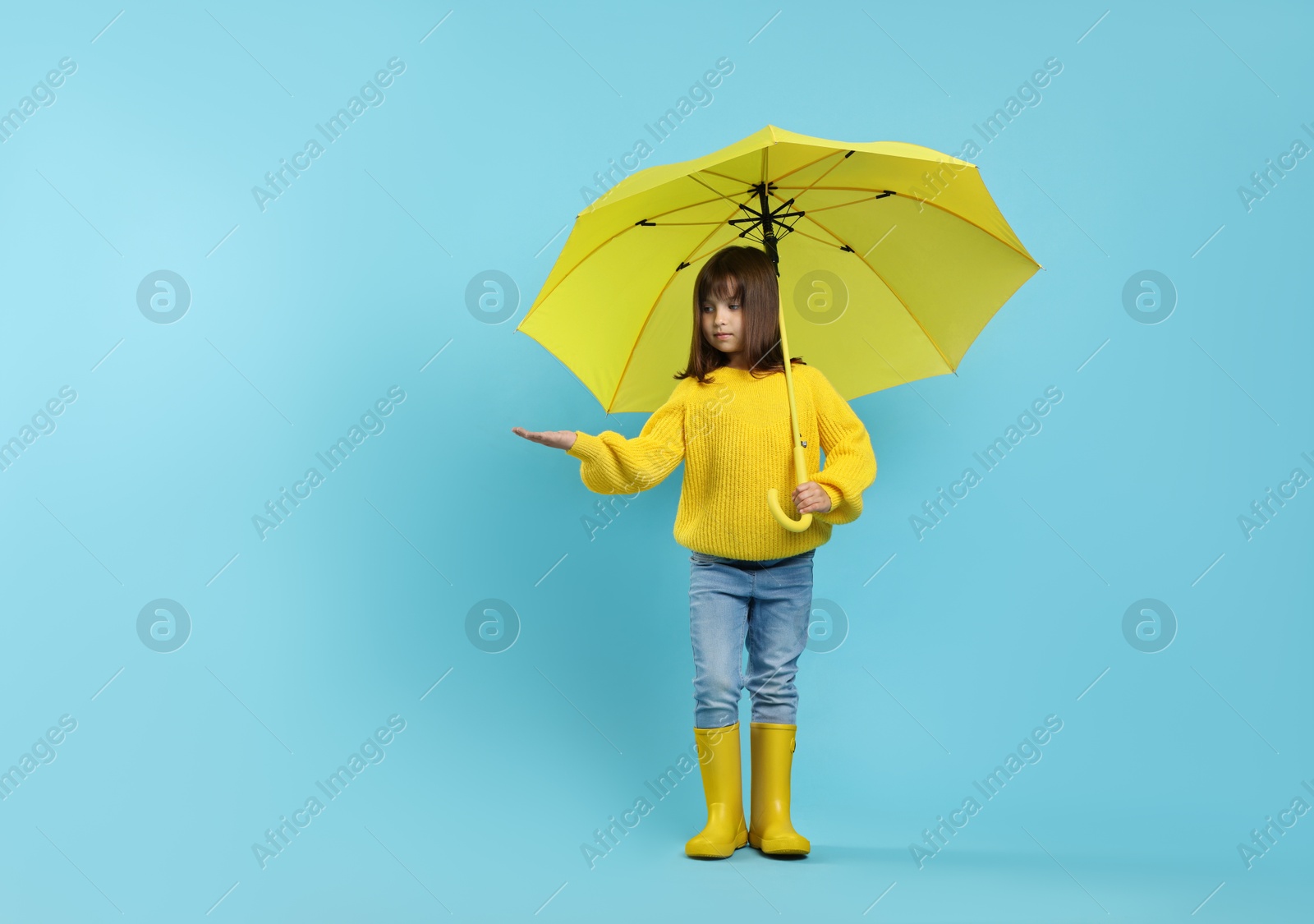 Photo of Cute little girl with yellow umbrella on light blue background