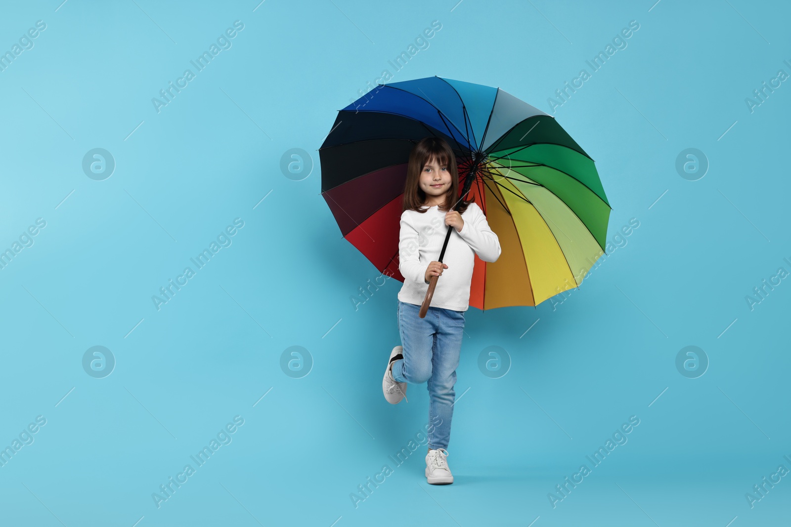 Photo of Cute little girl with colorful umbrella on light blue background. Space for text